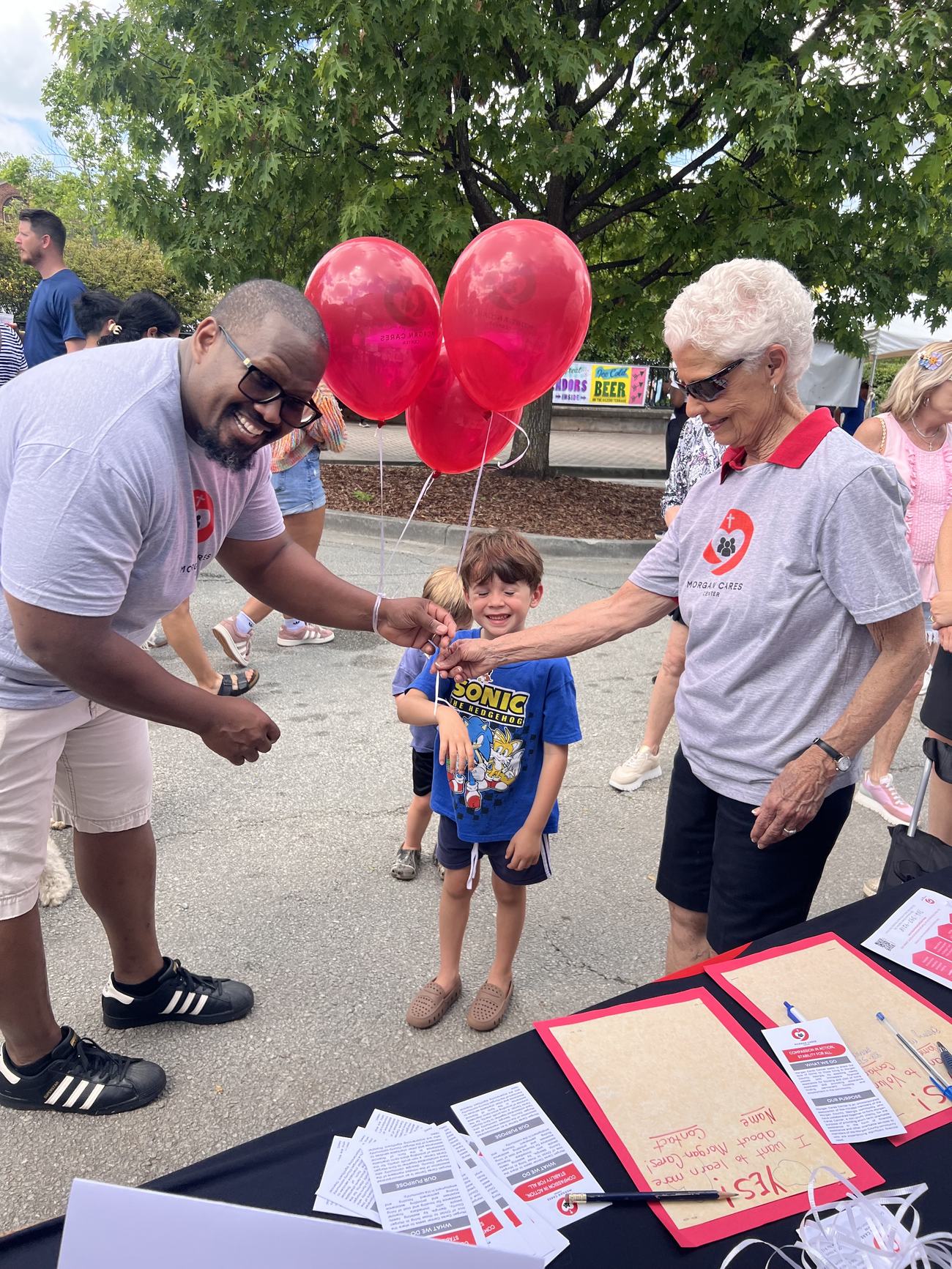 A Morgan Cares Center volunteer ties a red balloon to a child's wrist at a community festival in downtown Madison.
